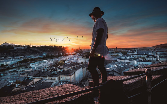 Mann in Trachtenkleidung steht auf einer Anhöhe und überblickt die Stadt Salzburg | © Ömer Karakus @ Pexels